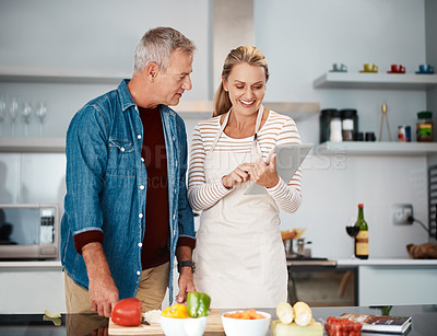 Buy stock photo Shot of a couple looking at a digital tablet while cooking in the kitchen