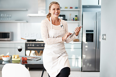 Buy stock photo Shot of a mature woman using her digital tablet while wearing her apron in the kitchen