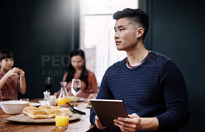 Buy stock photo Shot of a young family having a meal together while the father uses a tablet at home