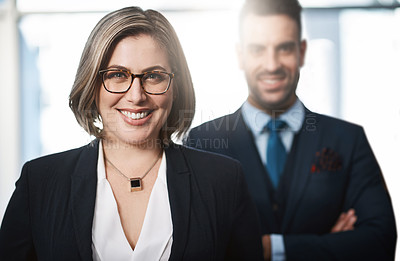 Buy stock photo Cropped portrait of an attractive young businesswoman standing in the office with a male colleague at her back