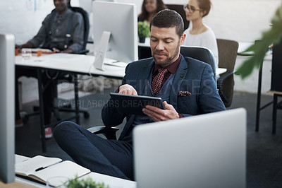 Buy stock photo Shot of a mature businessman using a digital tablet at his desk in a modern office