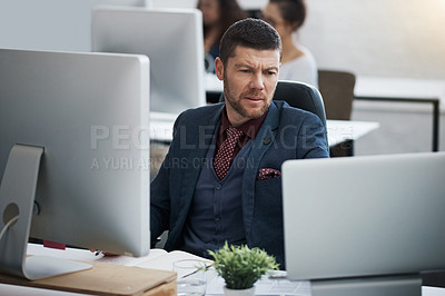 Buy stock photo Shot of a mature businessman using a computer and laptop at his desk in a modern office