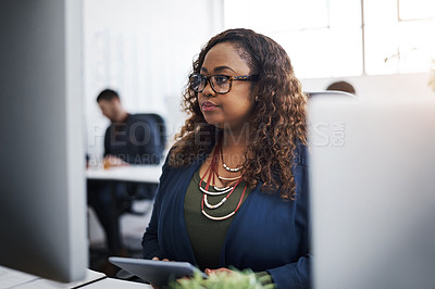 Buy stock photo Shot of a young businesswoman using a computer and digital tablet at her desk in a modern office