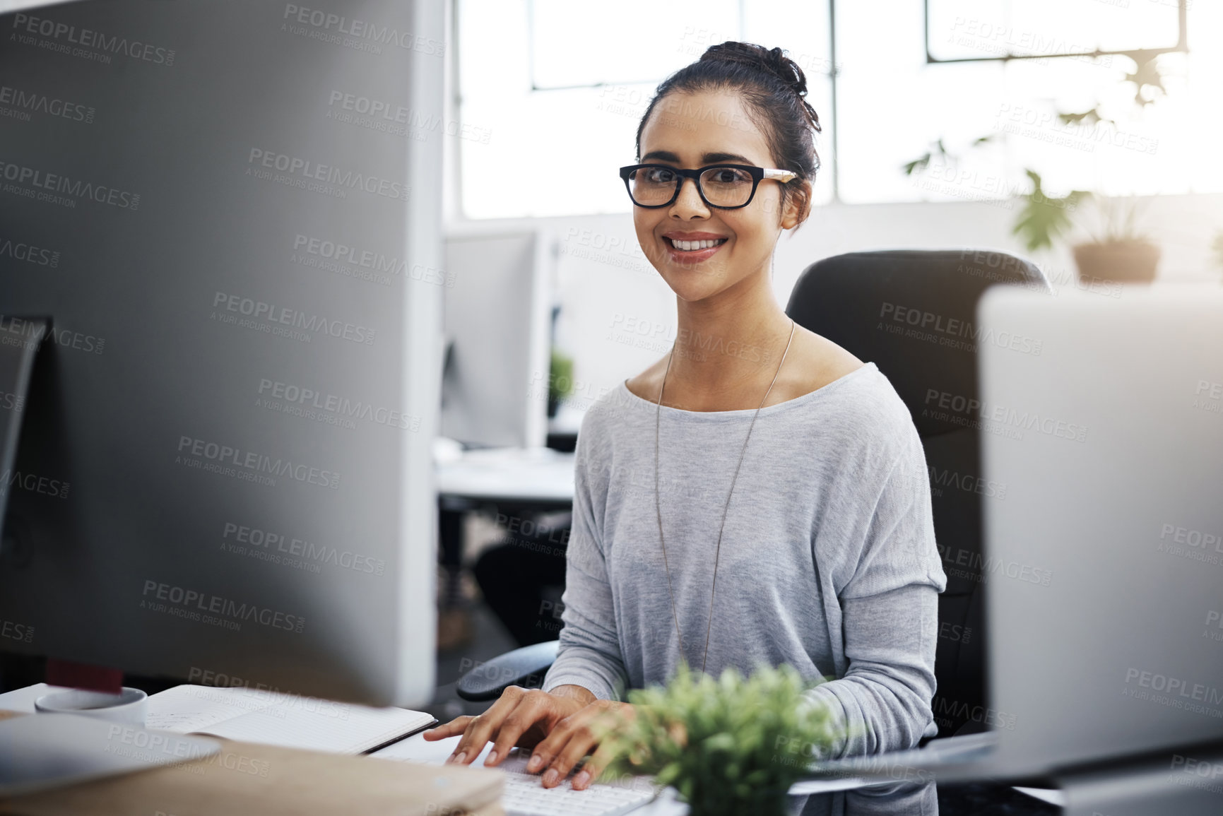 Buy stock photo Shot of a young businesswoman using a computer at her desk in a modern office
