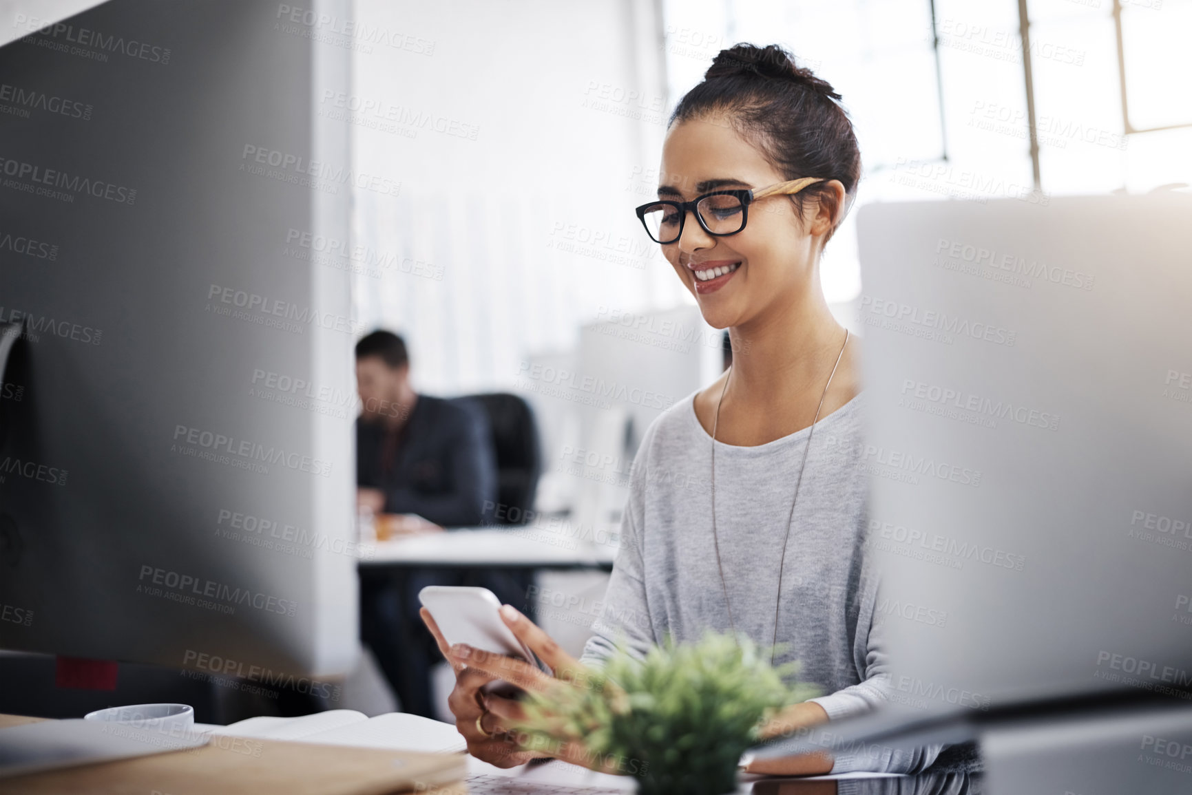 Buy stock photo Shot of a young businesswoman using a mobile phone at her desk in a modern office