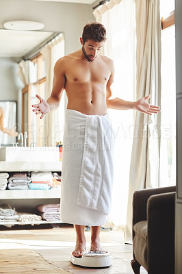 Buy stock photo Full length shot of a young man looking surprised while weighing himself in his bathroom at home