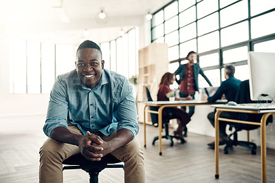 Buy stock photo Portrait of a young businessman sitting in a modern office with his colleagues working in the background