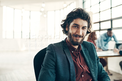 Buy stock photo Portrait of a young businessman sitting in a modern office with his colleagues working in the background