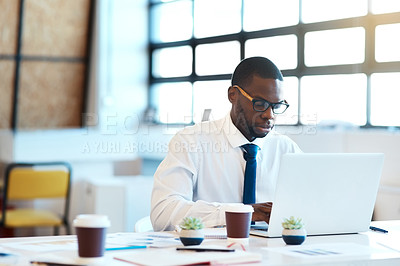 Buy stock photo Shot of a focused young businessman typing on his laptop while being seated at his desk in the office at work during the day