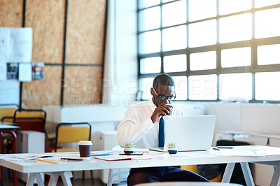 Buy stock photo Shot of a focused young businessman typing on his laptop and drinking coffee while being seated at his desk in the office at work during the day