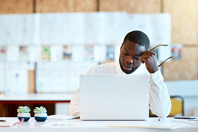 Buy stock photo Shot of a focused young businessman typing on his laptop and contemplating while being seated at his desk in the office at work during the day