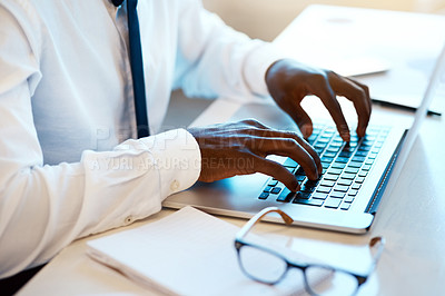 Buy stock photo Closeup of an unrecognizable man working and typing on his laptop at his desk with his reading glasses placed next to him in the office during the day