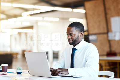 Buy stock photo Shot of a focused young businessman typing on his laptop while being seated at his desk in the office at work during the day