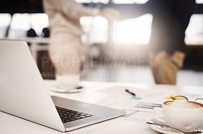 Buy stock photo Shot of a laptop on a table in an office with businesspeople shaking hands in the background