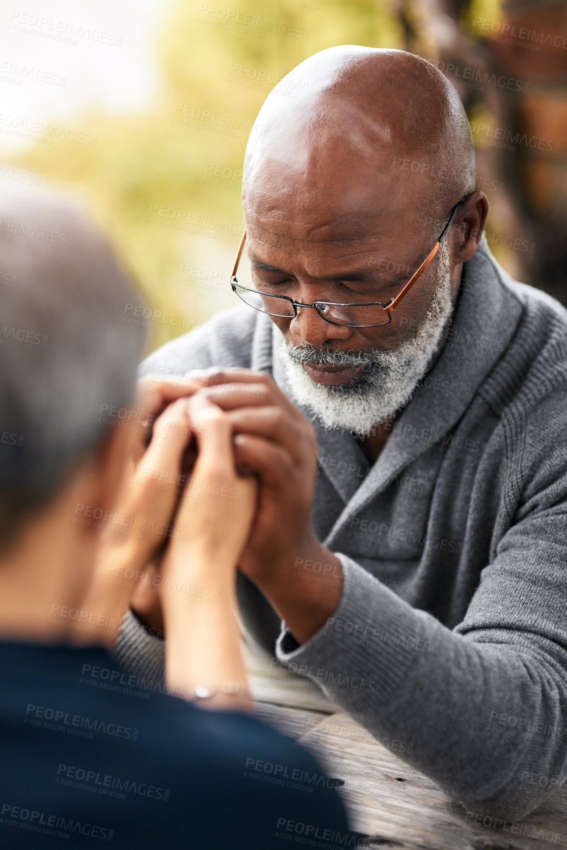 Buy stock photo Cropped shot of a senior couple holding hands in prayer while sitting outside
