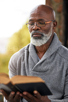 Buy stock photo Cropped shot of a handsome senior man reading his bible while sitting outside