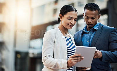 Buy stock photo Shot of two businesspeople using a digital tablet in the city
