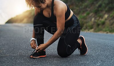 Buy stock photo Shot of a sporty young woman tying her laces while exercising outdoors