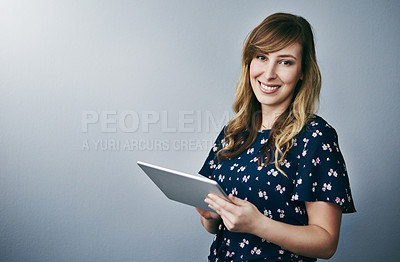 Buy stock photo Studio portrait of an attractive young woman using her digital tablet against a grey background