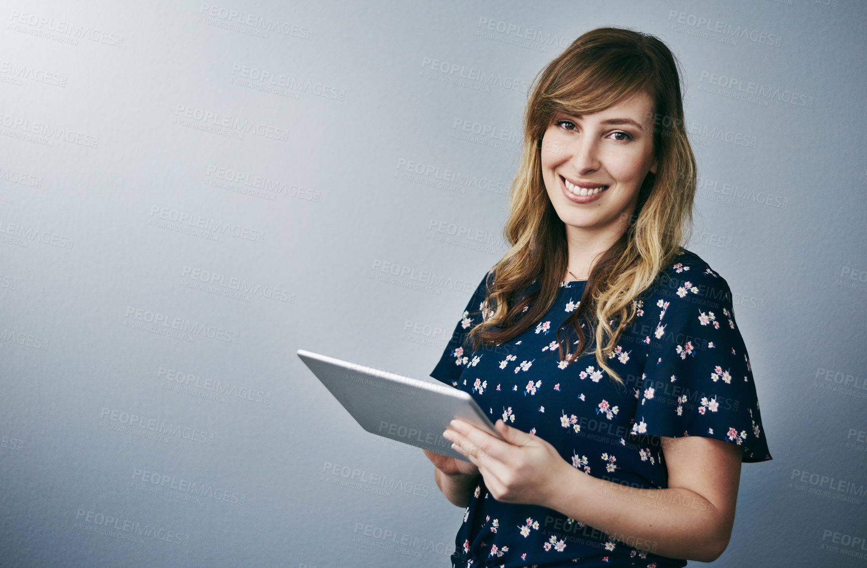 Buy stock photo Studio portrait of an attractive young woman using her digital tablet against a grey background