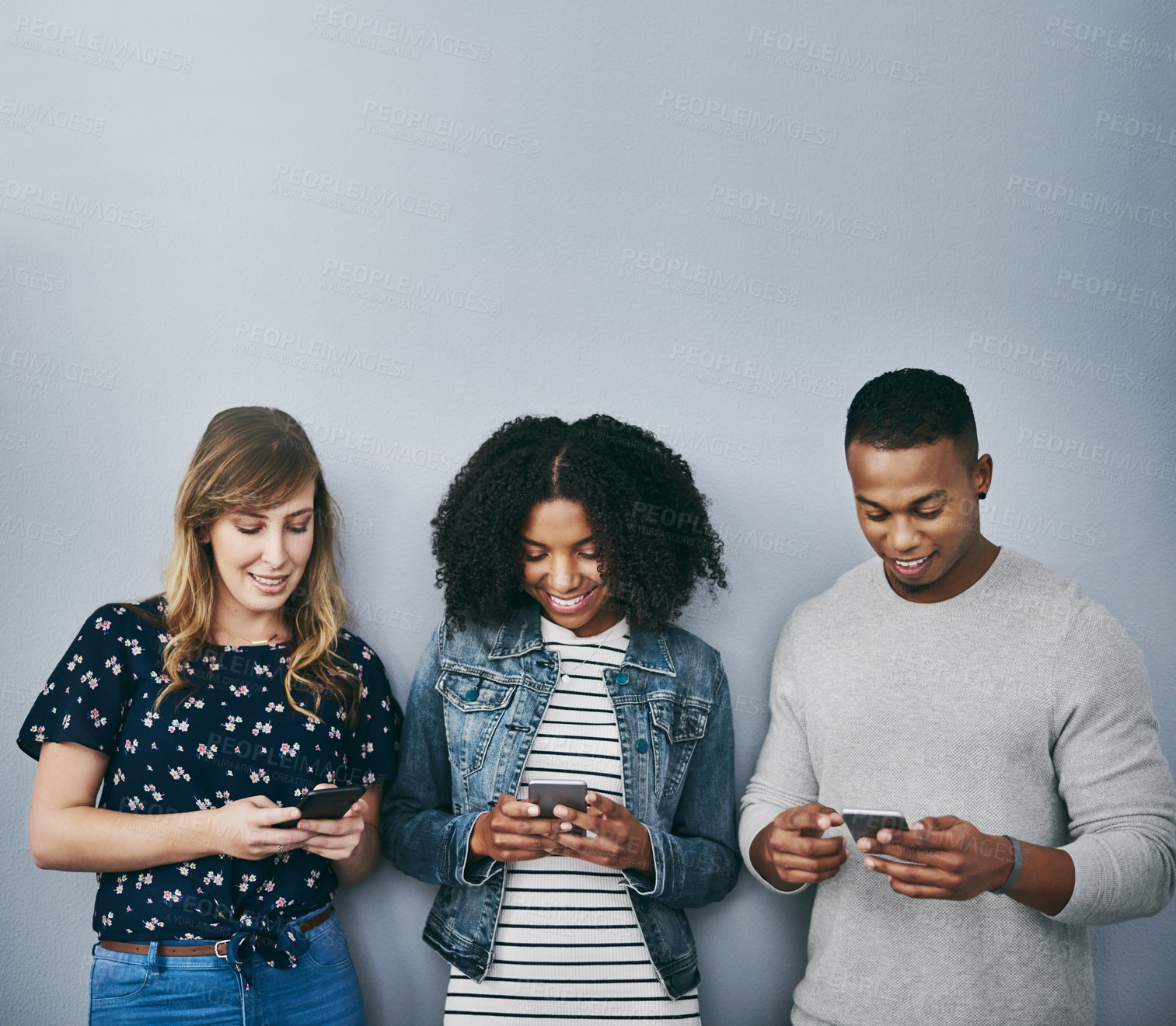 Buy stock photo Studio shot of three young people using their cellphones against a grey background