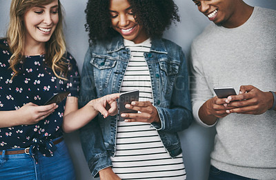 Buy stock photo Studio shot of three young people using their cellphones against a grey background