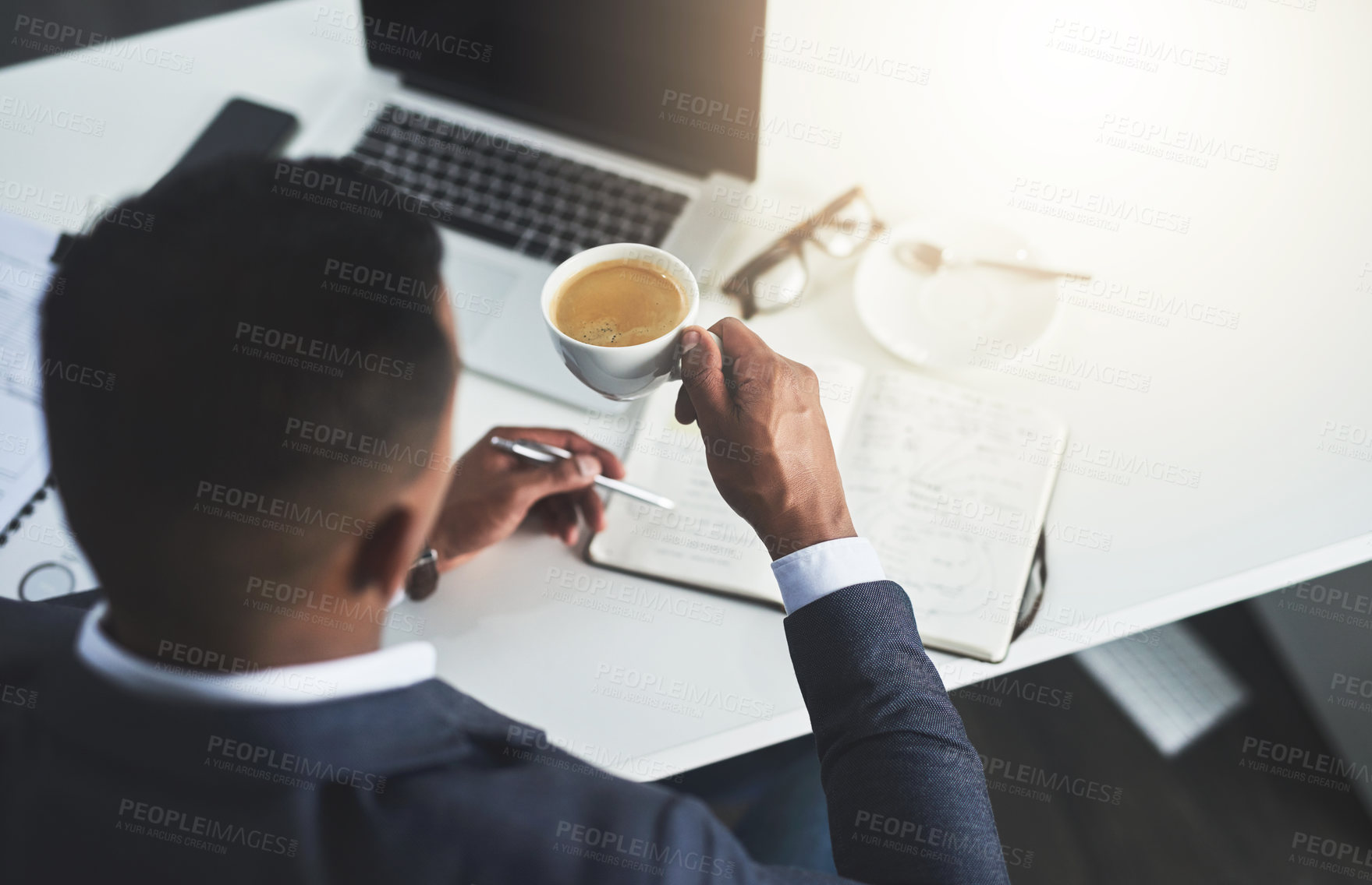 Buy stock photo High angle shot of an unrecognizable young businessman drinking coffee while working in his modern office