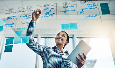 Buy stock photo Shot of a young businesswoman using a digital tablet while writing notes on a glass wall in an office