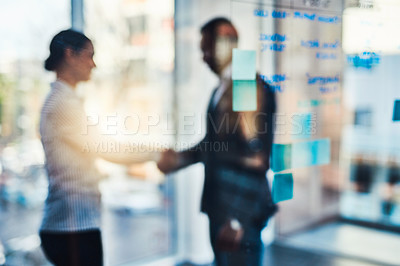 Buy stock photo Defocused shot of two businesspeople shaking hands in an office