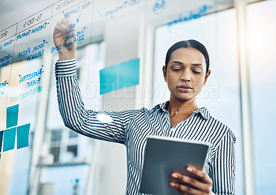 Buy stock photo Shot of a young businesswoman using a digital tablet while writing notes on a glass wall in an office