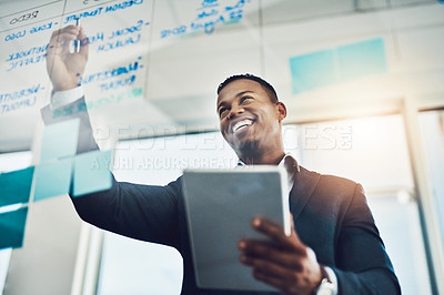 Buy stock photo Shot of a young businessman using a digital tablet while writing notes on a glass wall in an office