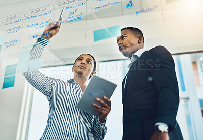 Buy stock photo Shot of two businesspeople brainstorming with notes on a glass wall in an office