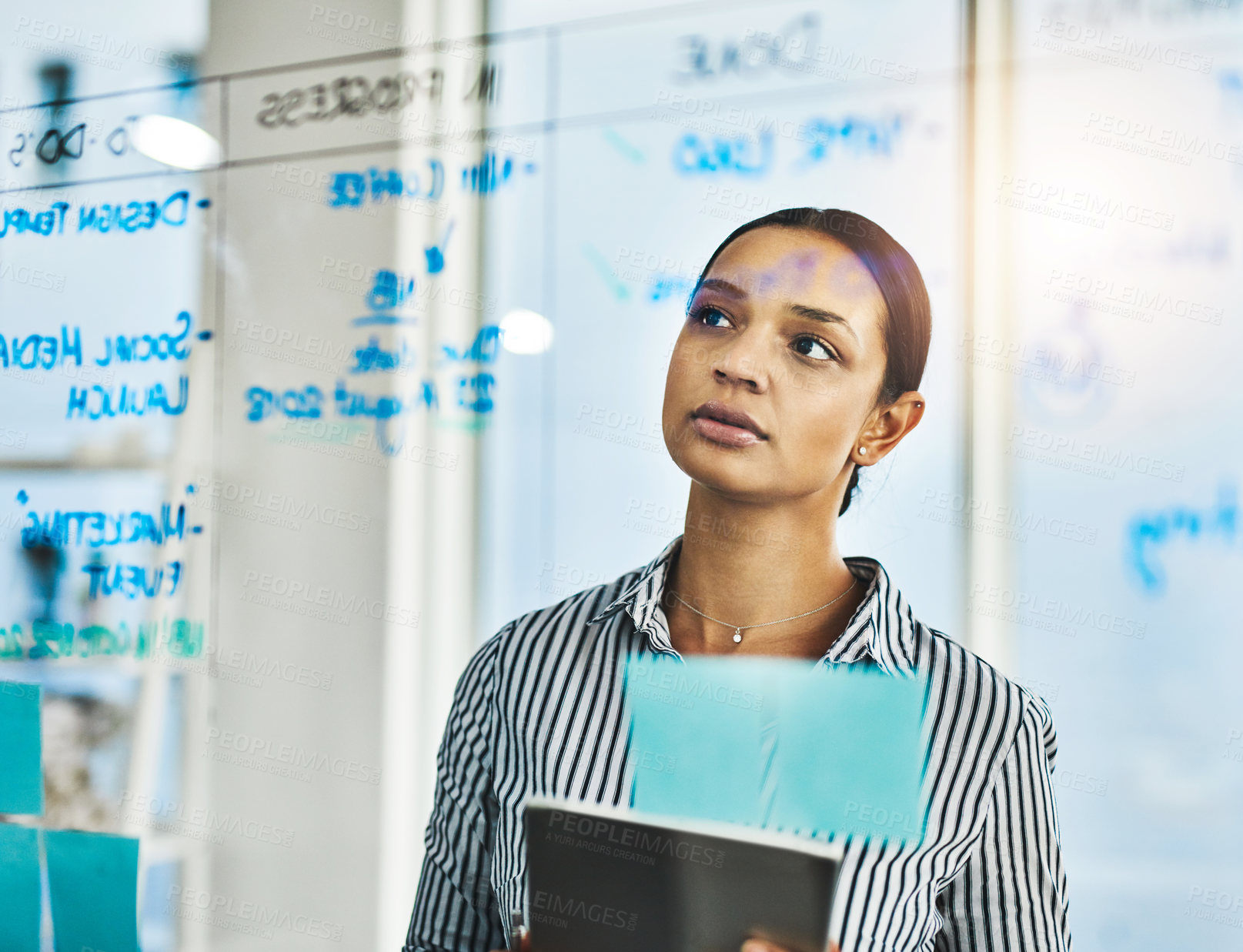 Buy stock photo Shot of a young businesswoman using a digital tablet while brainstorming on a glass wall in an office