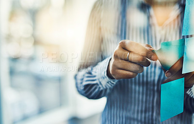 Buy stock photo Closeup shot of an unrecognizable businesswoman sticking adhesive notes onto a glass wall in an office