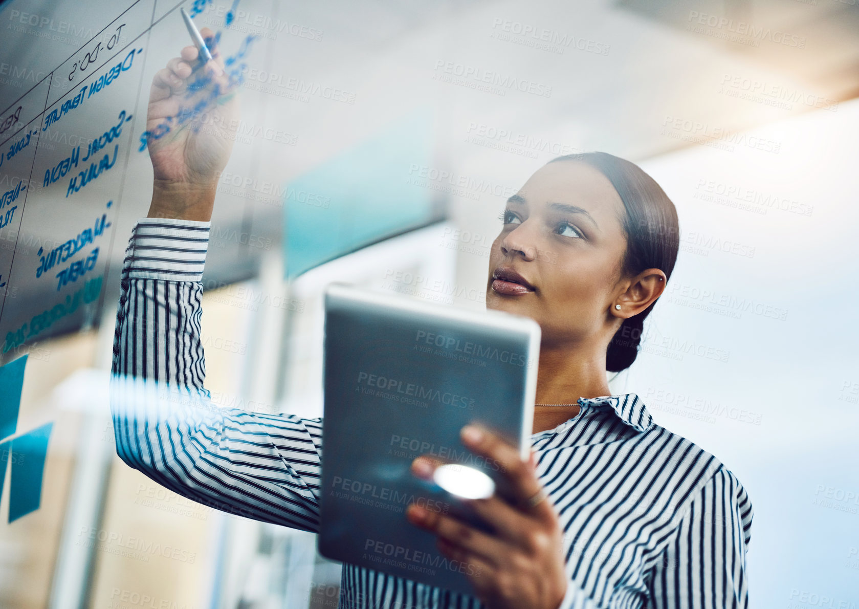 Buy stock photo Shot of a young businesswoman using a digital tablet while writing notes on a glass wall in an office