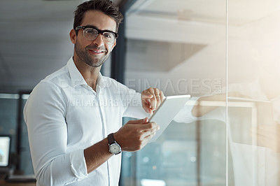 Buy stock photo Cropped portrait of a handsome young businessman working on his digital tablet while standing in the office