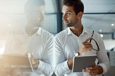 Buy stock photo Cropped shot of a handsome young businessman looking thoughtful working on his digital tablet while standing in the office