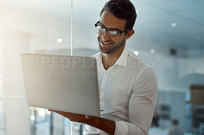 Buy stock photo Cropped shot of a handsome young businessman working on his laptop while standing in the office