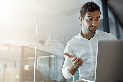 Buy stock photo Cropped shot of a handsome young businessman looking unsure while working on his laptop in the office