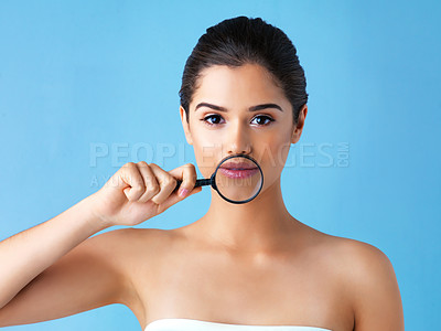 Buy stock photo Studio portrait of a beautiful young woman holding a magnifying glass against a blue background