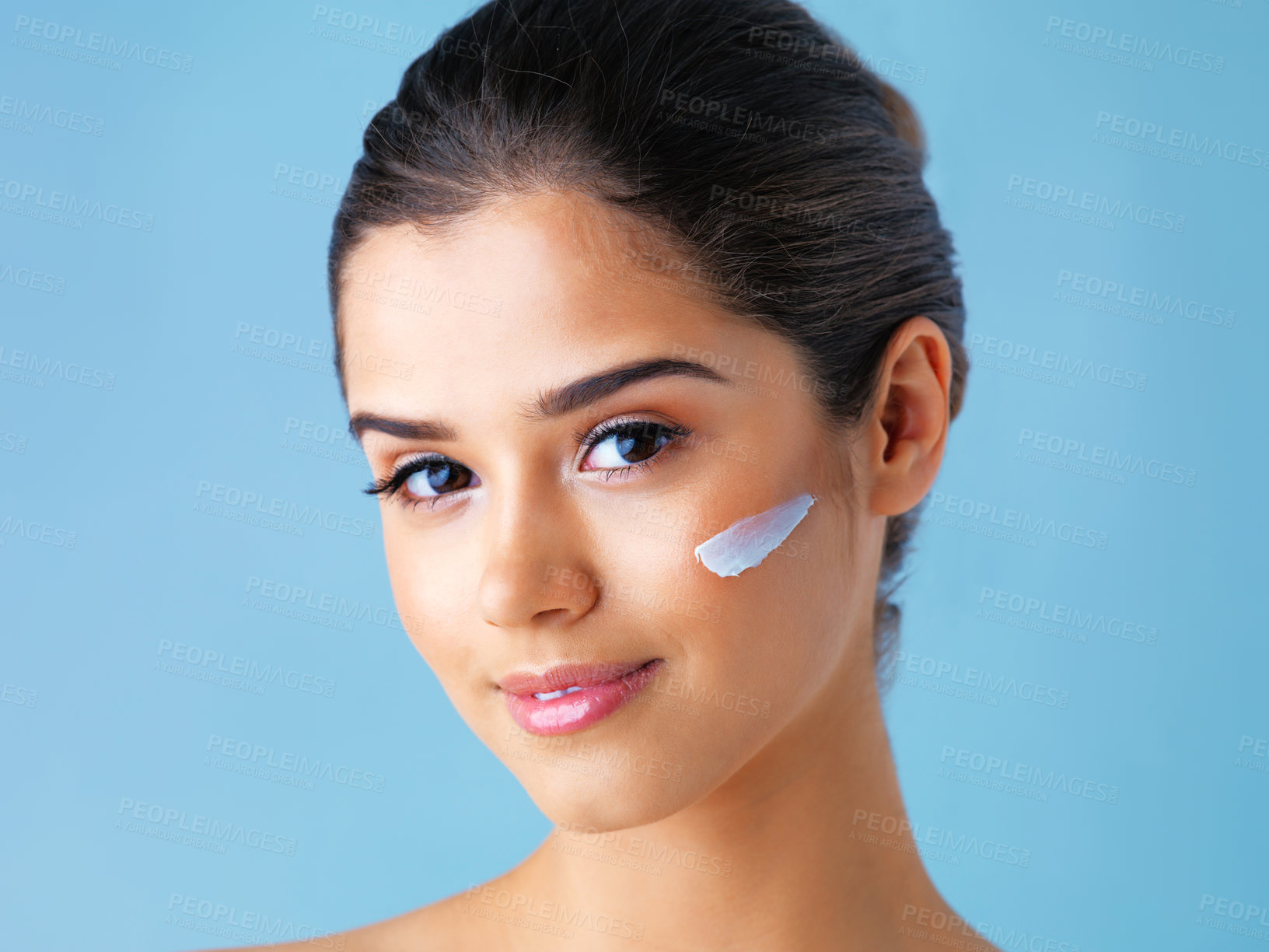 Buy stock photo Studio portrait of a beautiful young woman with lotion on her face against a blue background