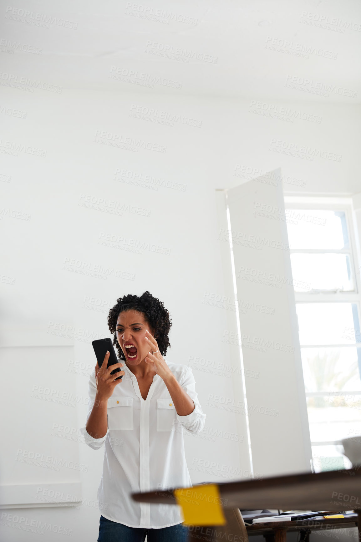 Buy stock photo Cropped shot of a young businesswoman shouting at her cellphone in anger at the office