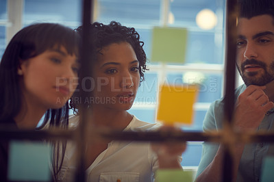 Buy stock photo Cropped shot of young businesspeople brainstorming on a glass wall in the office