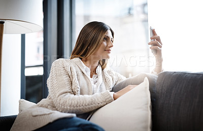 Buy stock photo Shot of a beautiful young woman using her cellphone while relaxing at home