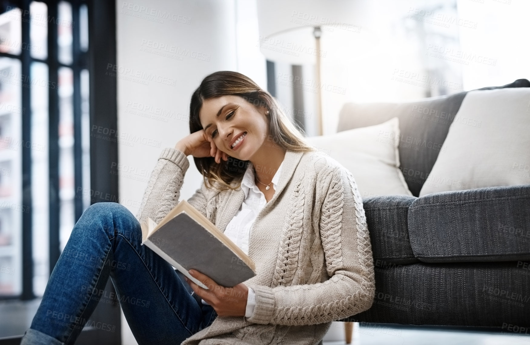 Buy stock photo Cropped shot of a beautiful young woman reading a book while relaxing at home