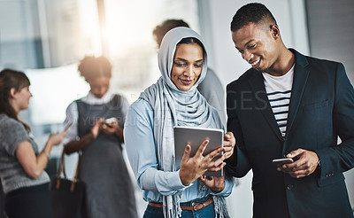 Buy stock photo Shot of a group of young cheerful businesspeople browsing on digital devices while working together in the office at work