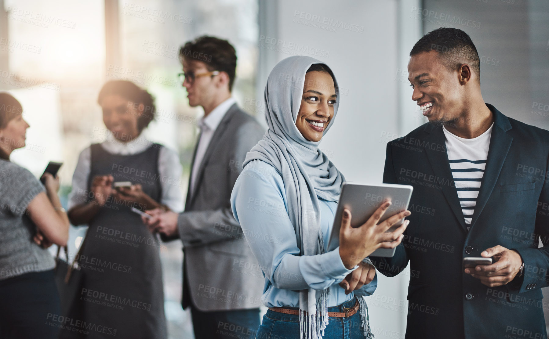 Buy stock photo Shot of a group of young cheerful businesspeople browsing on digital devices while working together in the office at work