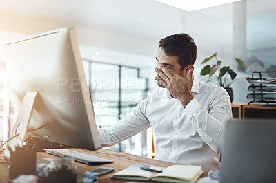 Buy stock photo Shot of a young businessman looking stressed out and tired while working in an office