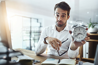 Buy stock photo Portrait of a young businessman looking stressed out while holding a clock in an office