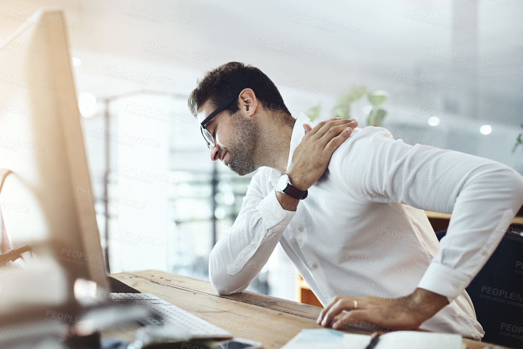 Buy stock photo Shot of a young businessman suffering with shoulder pain while working in an office